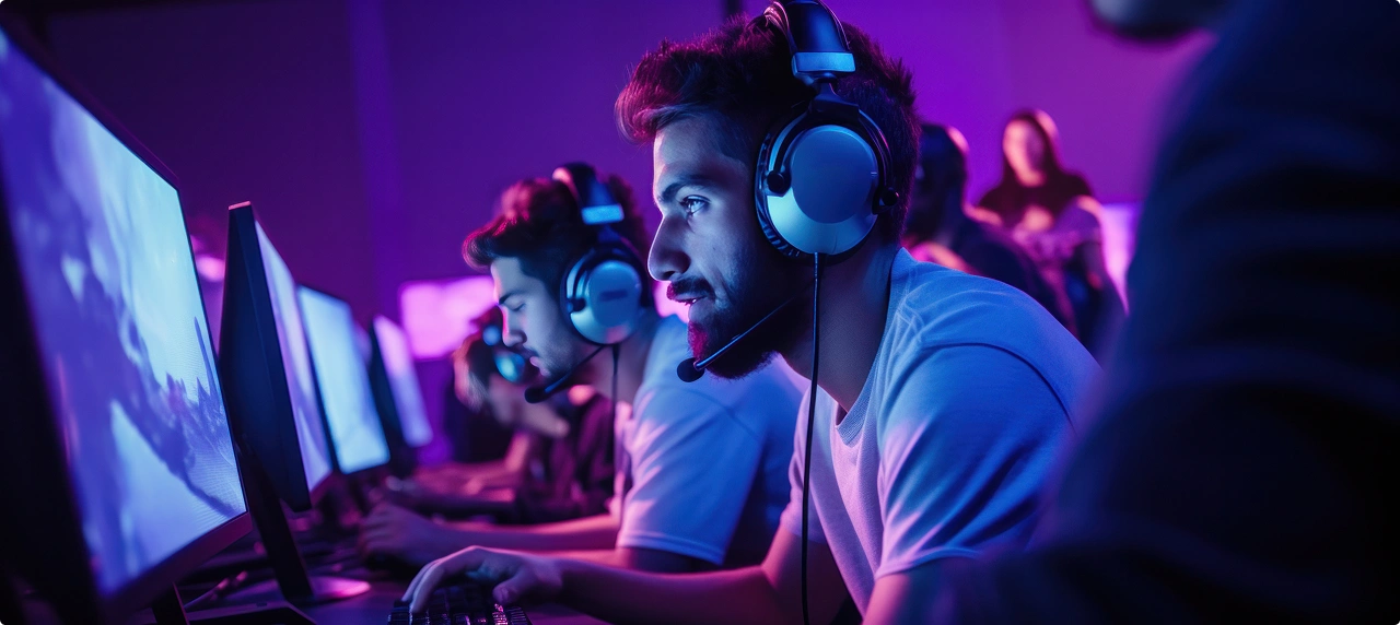 Fejhallgatóval felszerelt játékosok a számítógépük előtt játszanak egy neonfényben úszó e-sport-versenyen.