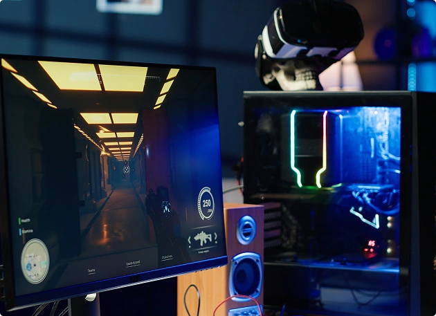 Egy átlátszó házú, RGB-megvilágítású játékgép, mellette egy monitor, amelyen egy videojáték fut.