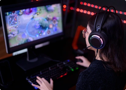 Egy fejhallgatót viselő női játékos RGB-megvilágítású számítógépen online játékot játszik.